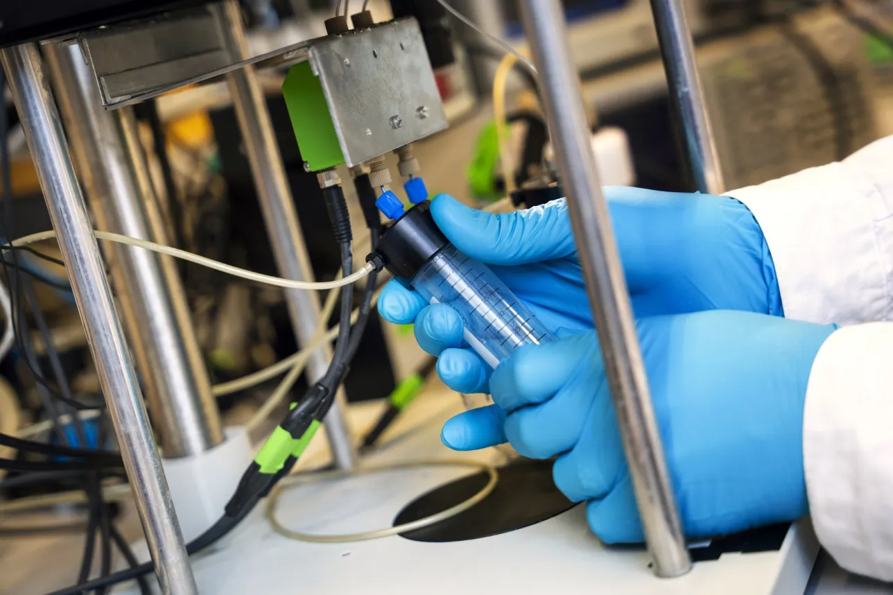Gloved hands mounting a test tube to a setup. Photo.