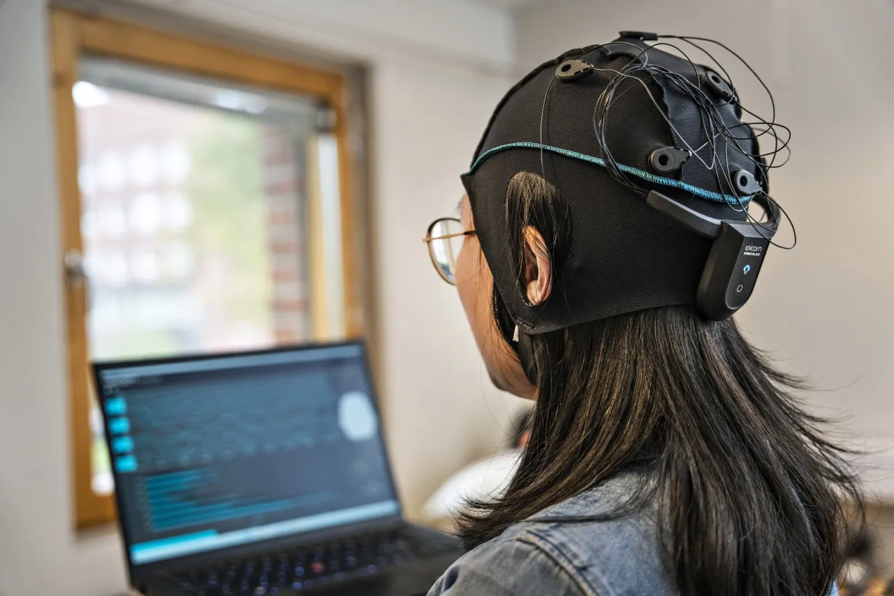 Woman wearing head electrode cap in front of a computer screen. Photo.